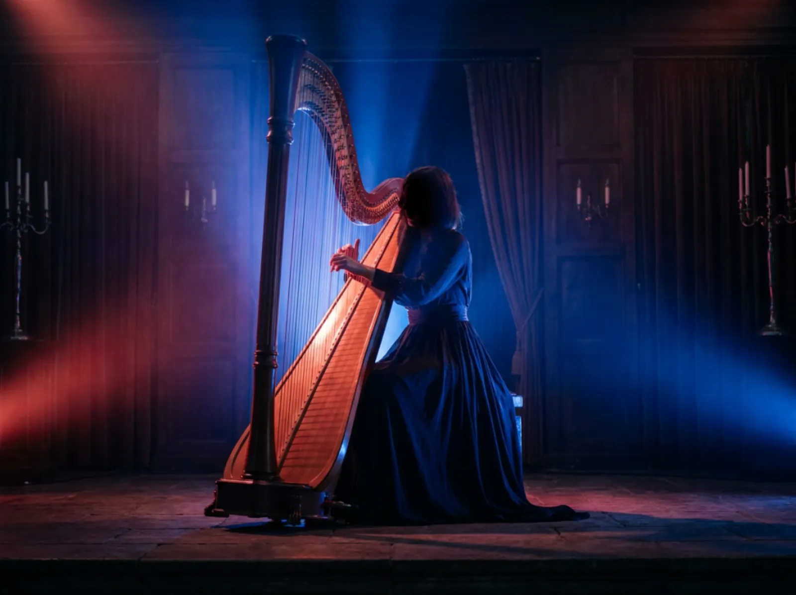 Harpist lit by blue and red light in a dark setting
